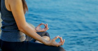 The woman meditating in a yoga pose on the tropical beach. Female meditating overlooking the beautiful sunrise. Healthy mind body and spirit concept.